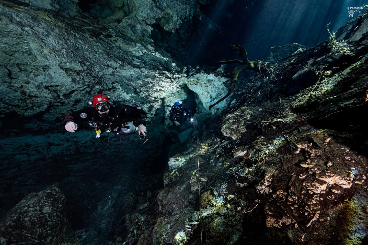 A cave diver following a guideline as light beams stream down from an opening above