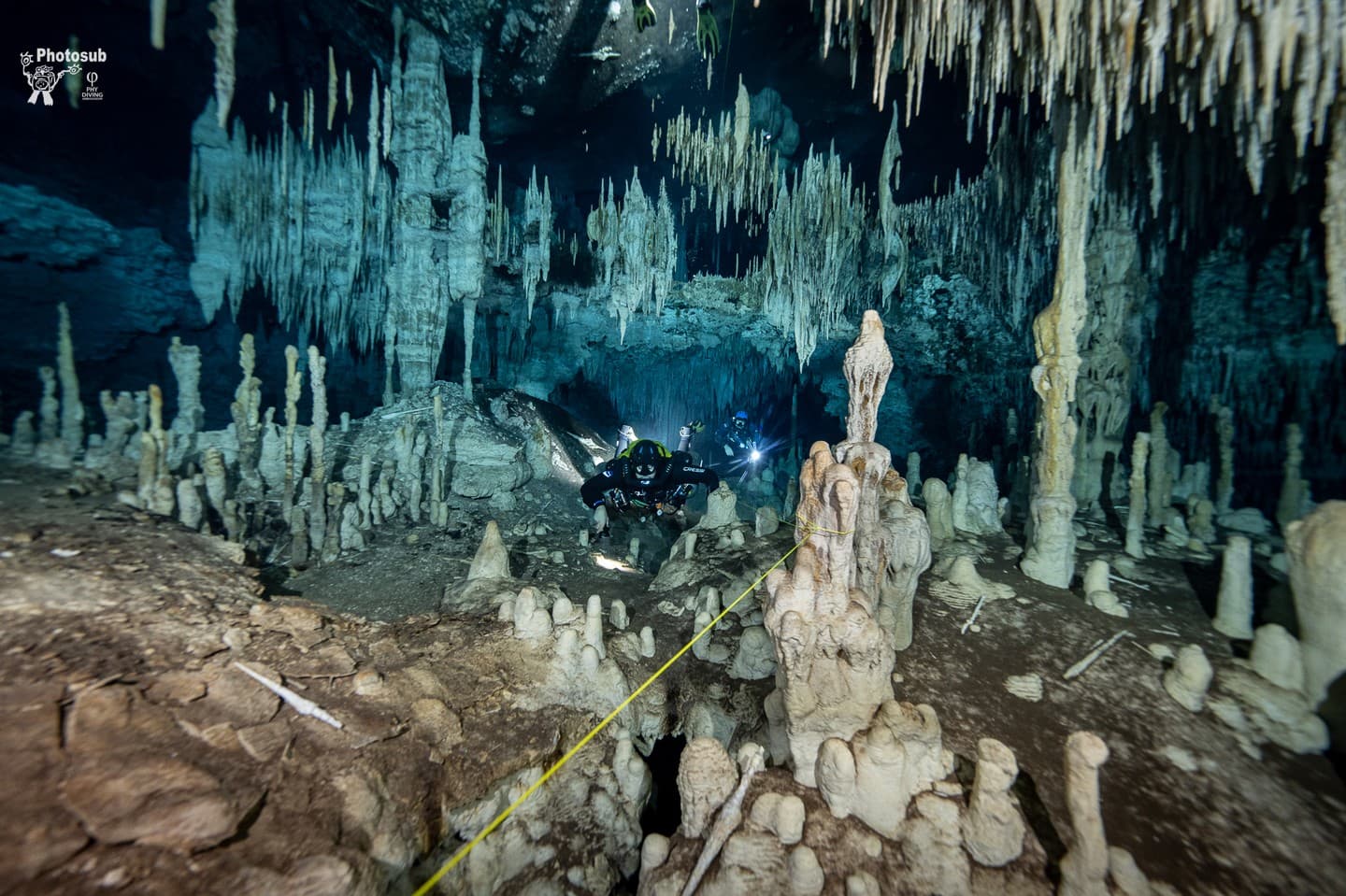Diver in a decorated cave chamber of stalactites and stalagmites with a yellow guideline