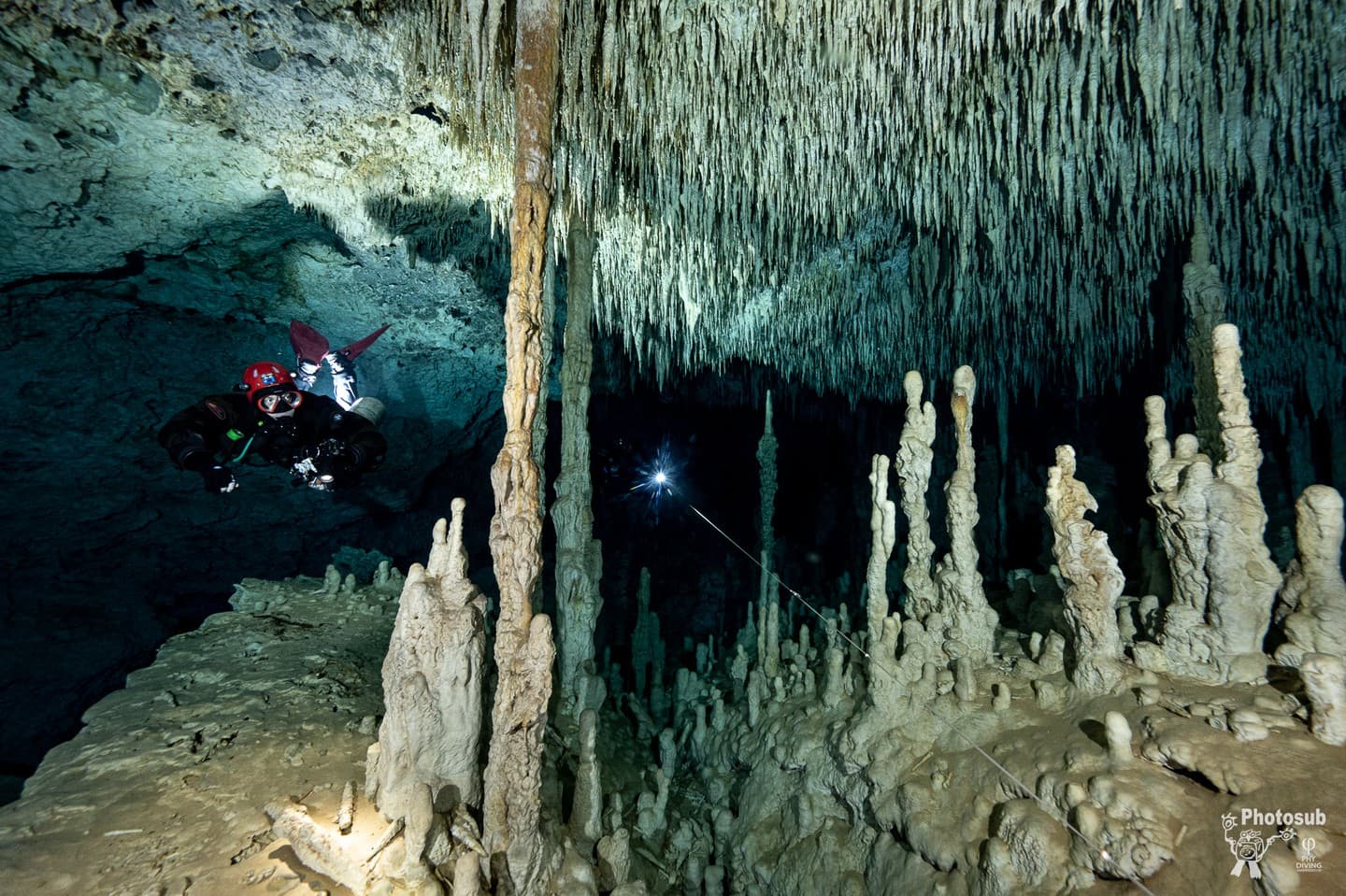 A cave diver lighting a chamber filled with dense stalactite and stalagmite formations