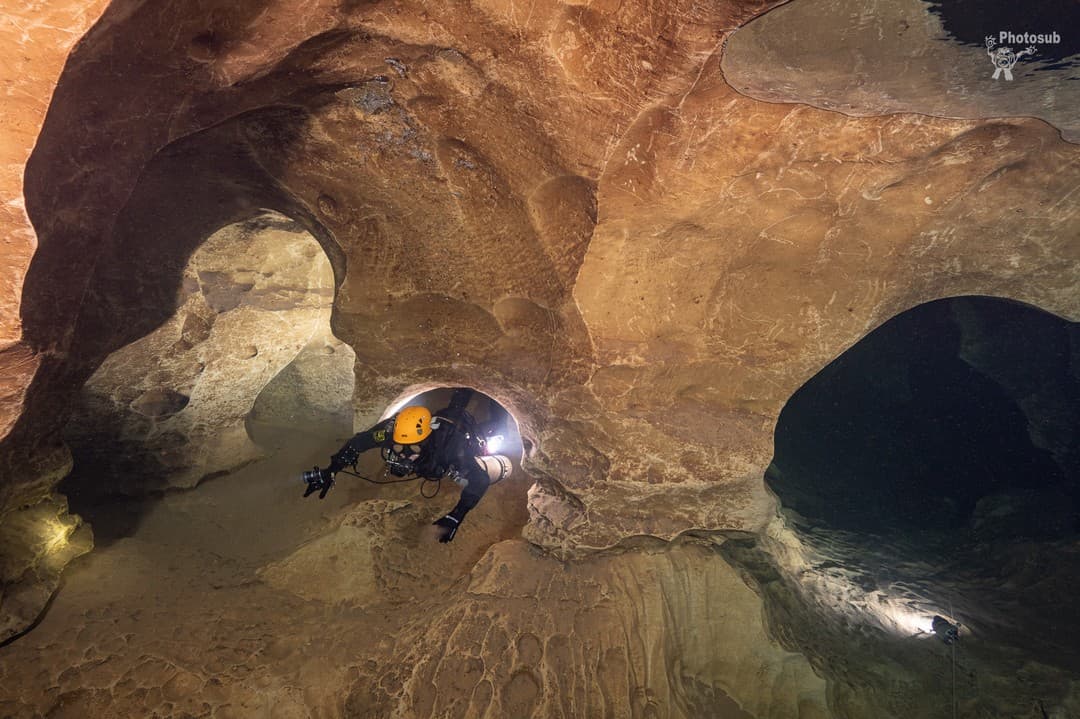 Cave diver in a chamber of sculpted limestone with several arches and dark side passages branching off