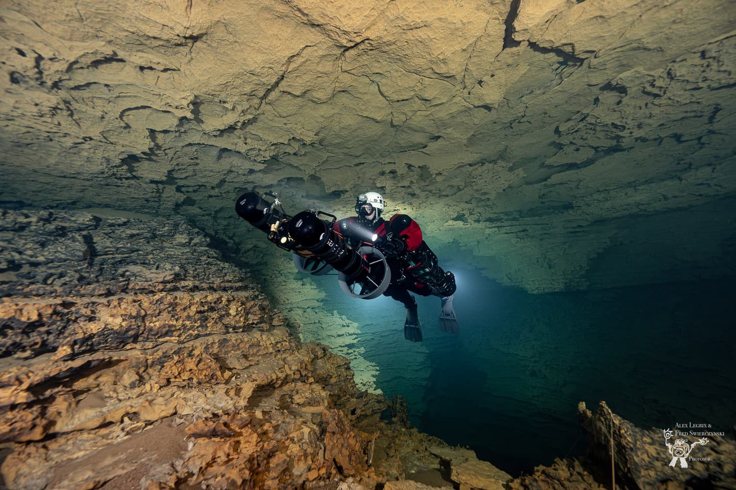 Two divers in dual Liberty Sidemount rebreather configuration riding DPVs side by side through a cave