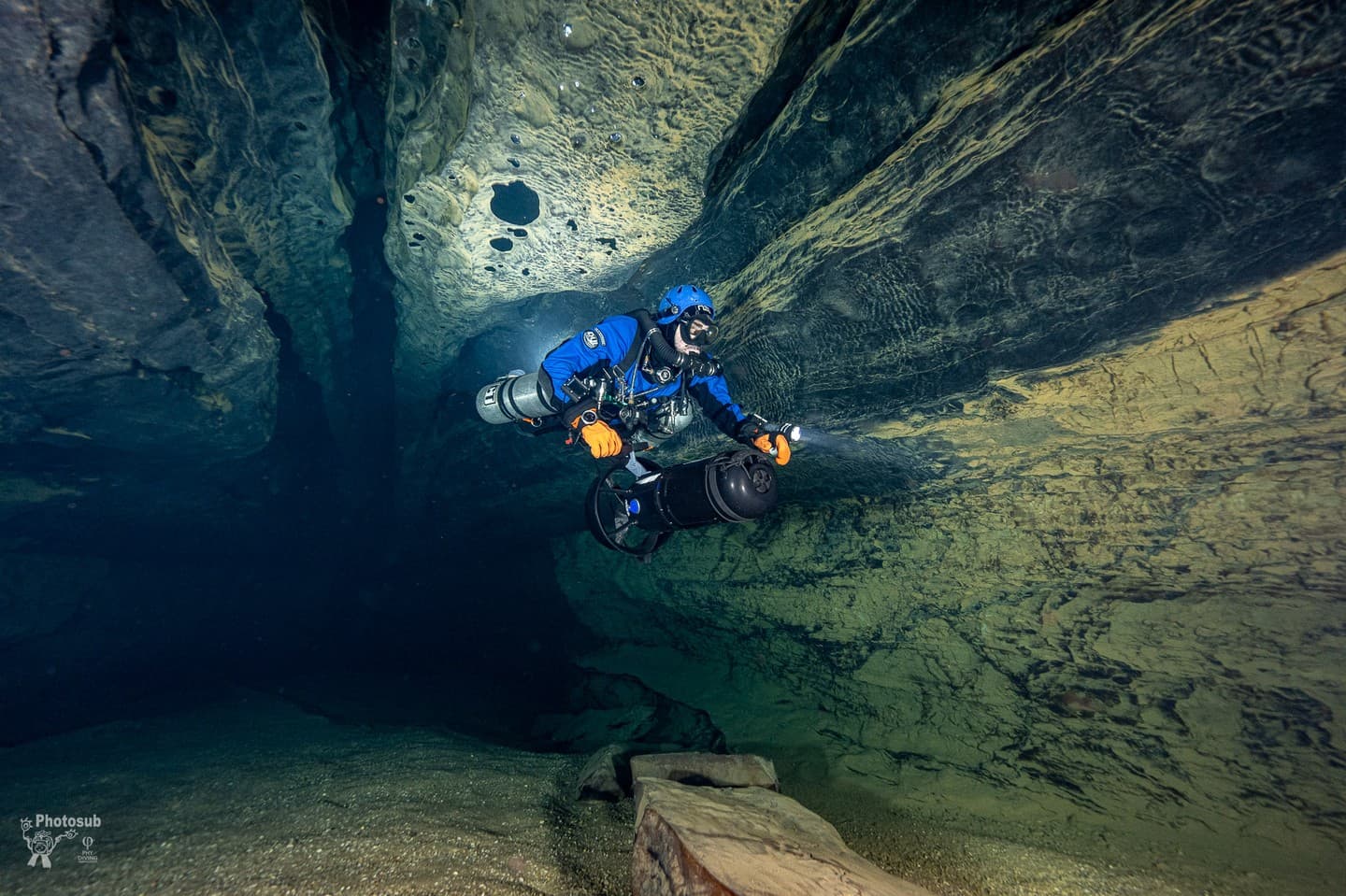Diver in dual sidemount rebreathers with a DPV in a cave passage