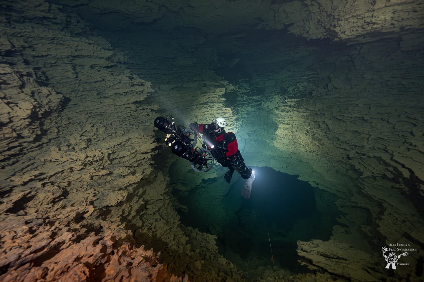 Diver in dual sidemount rebreathers descending into a cave with a DPV
