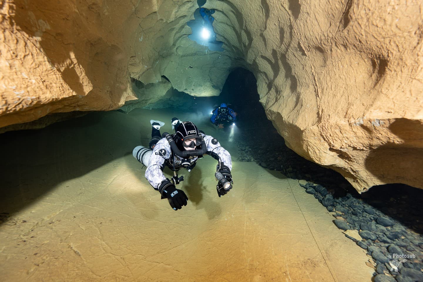 Diver in dual sidemount rebreathers leading a teammate through a low cave passage