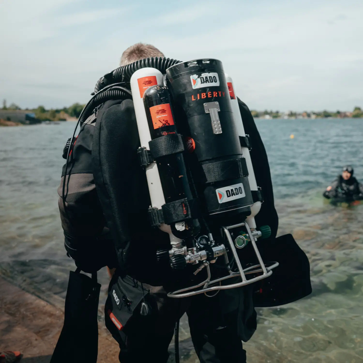 A diver geared up in the heavy twin-cylinder Liberty configuration at the water edge before a dive