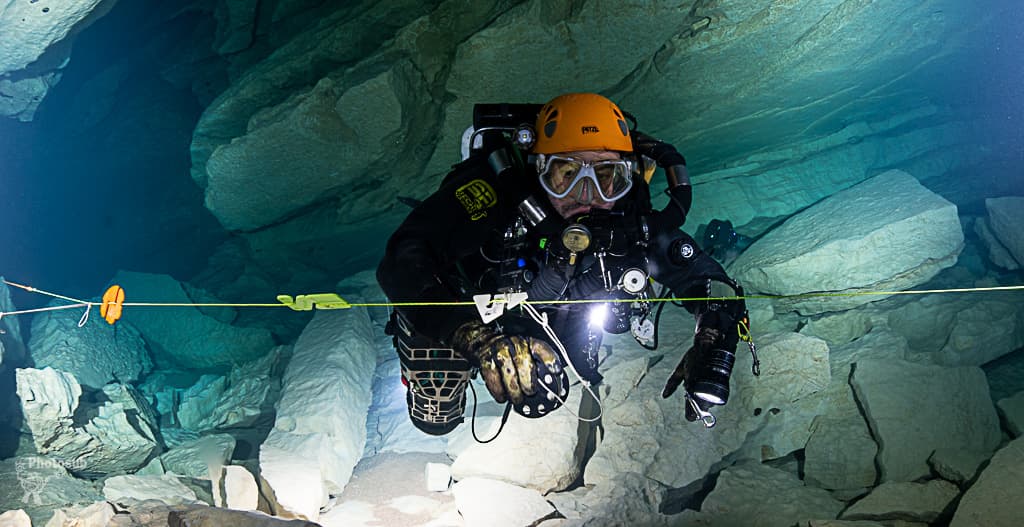 Diver checking a directional arrow marker on the guideline with spool in hand in a cave
