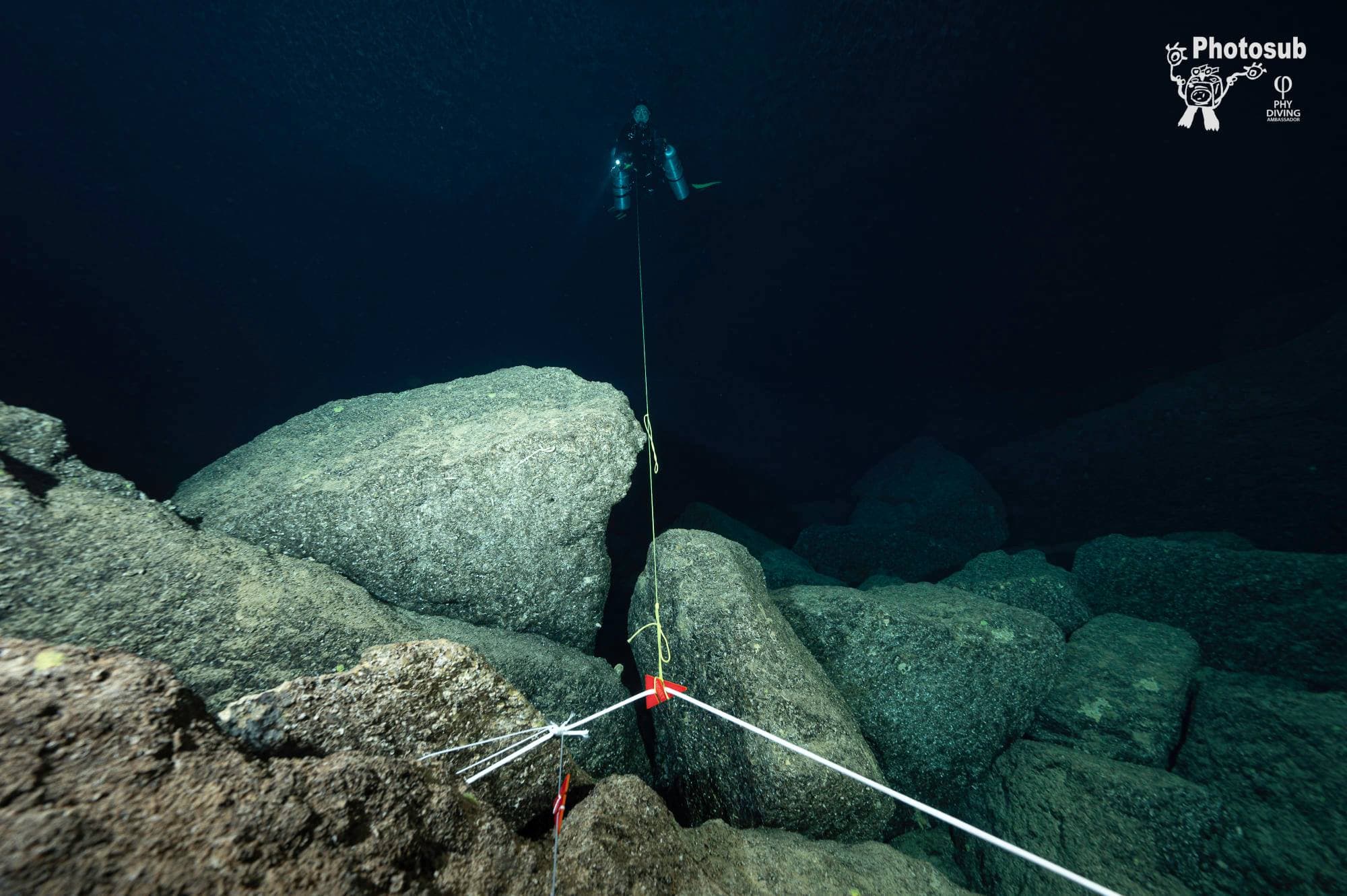 Guideline across boulders with a red directional arrow marker, diver descending on the line