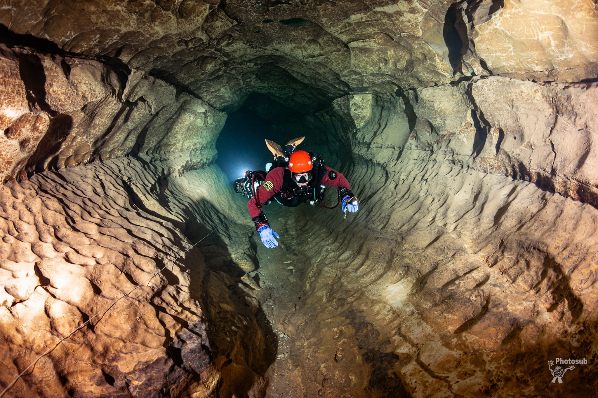 Cave diver holding flat horizontal trim while finning through a water-worn rock tunnel