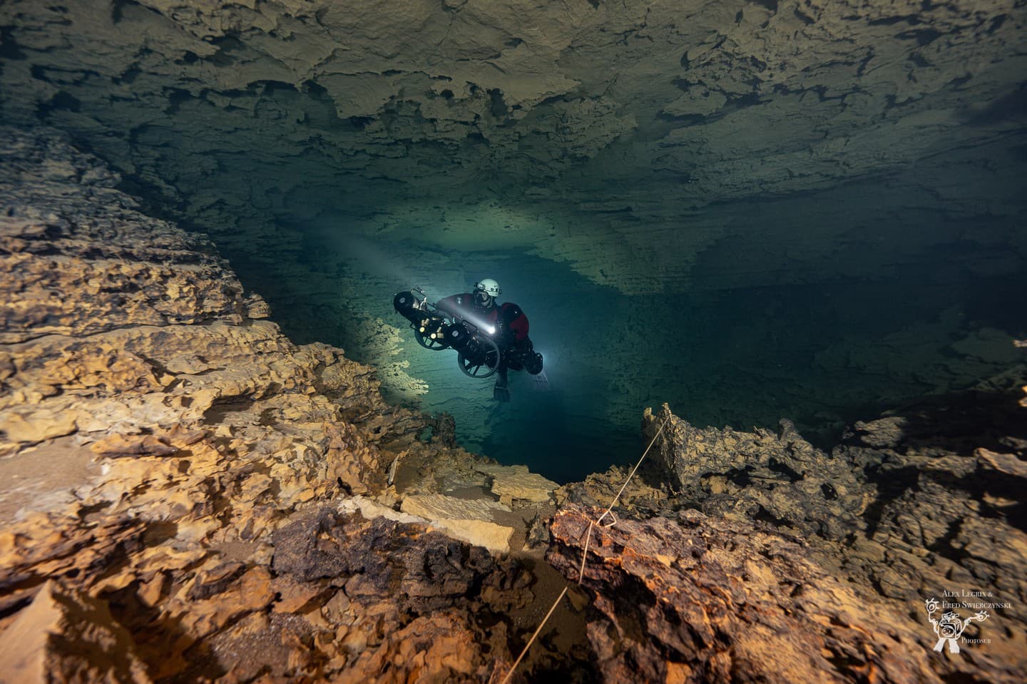A cave diver on a closed-circuit rebreather hovering above a guideline in a rocky chamber