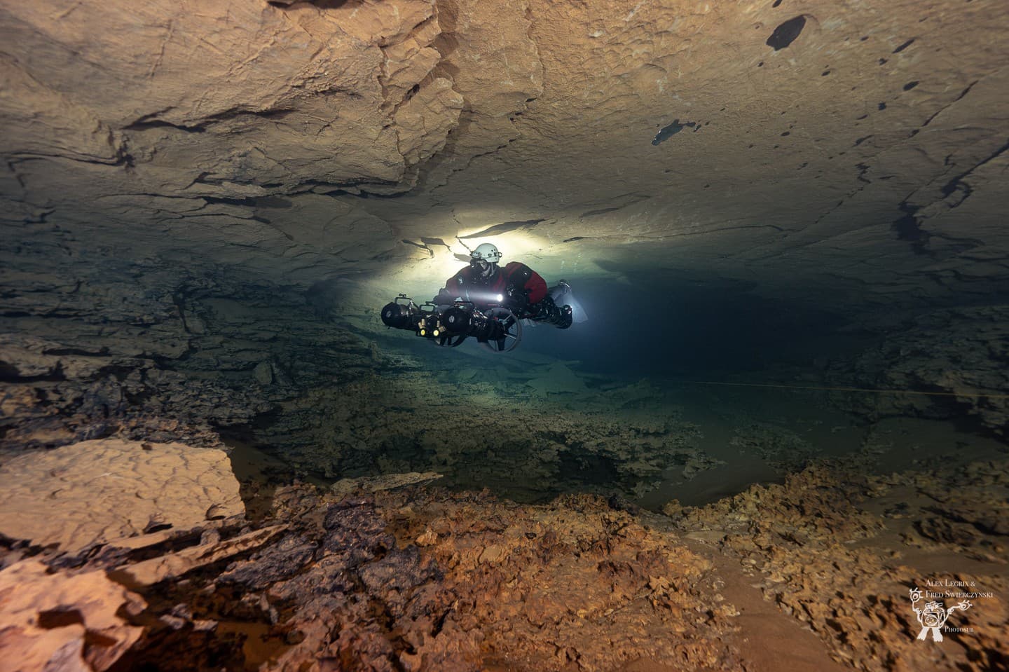 A rebreather diver holding a diver propulsion vehicle while hovering in a wide low cave passage