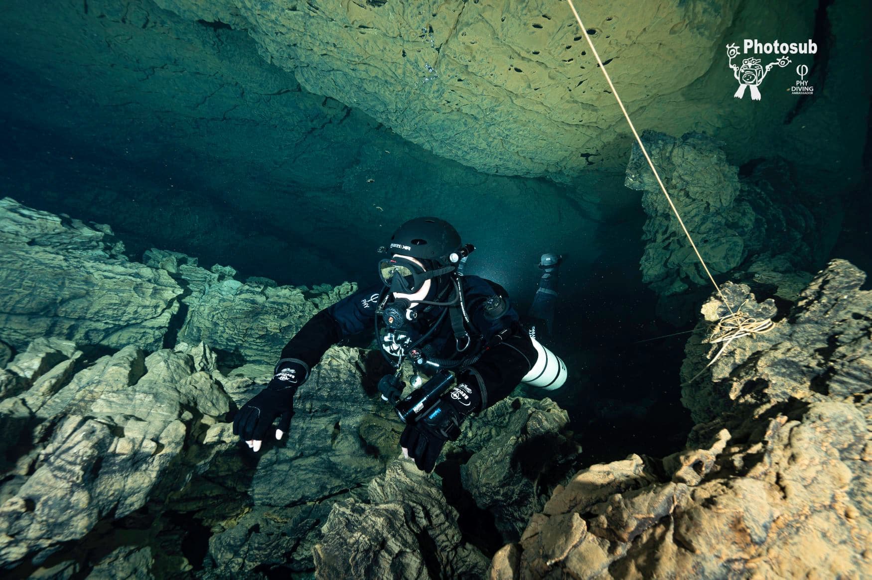 Diver in open-circuit sidemount configuration following a guideline along a cave wall