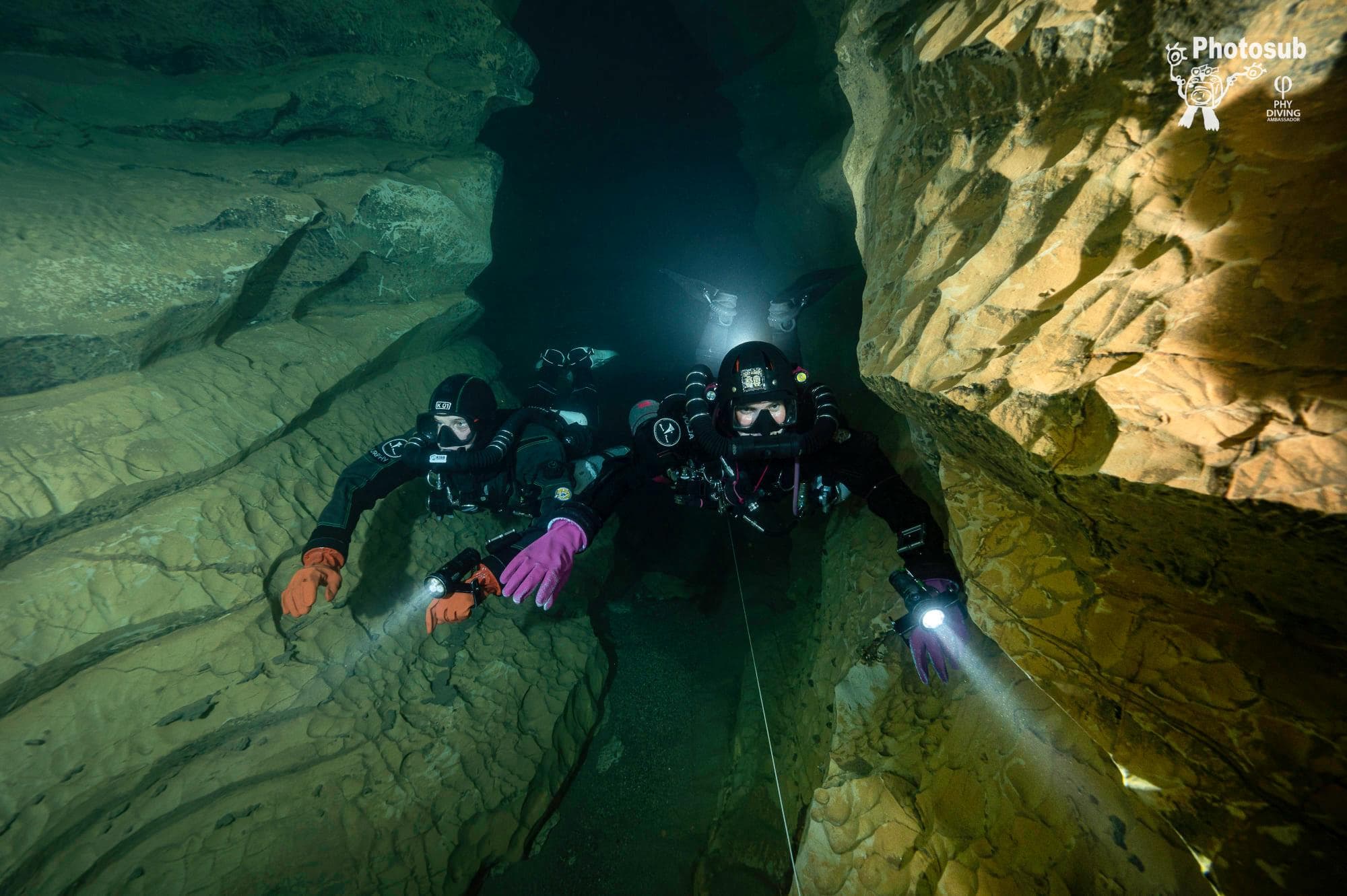 Two rebreather divers moving together as a team through a narrow cave passage